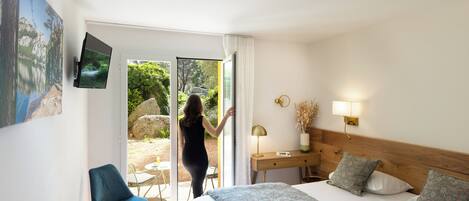 Habitación de hotel con cama, escritorio, silla, televisión y puerta corrediza de vidrio que da a un espacio al aire libre.