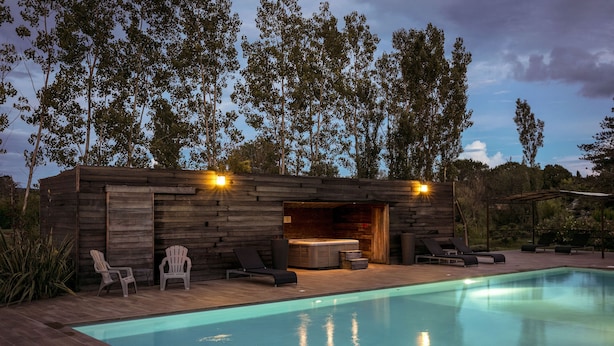 A modern outdoor pool area with a wooden deck, lounge chairs, and a hot tub.