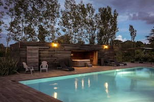 Un área de piscina moderna al aire libre con terraza de madera, sillas de descanso y un jacuzzi.