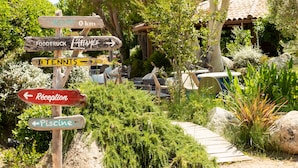 A wooden signpost with multiple directional signs pointing to various amenities such as a food truck, tennis court, reception, and a pool.
