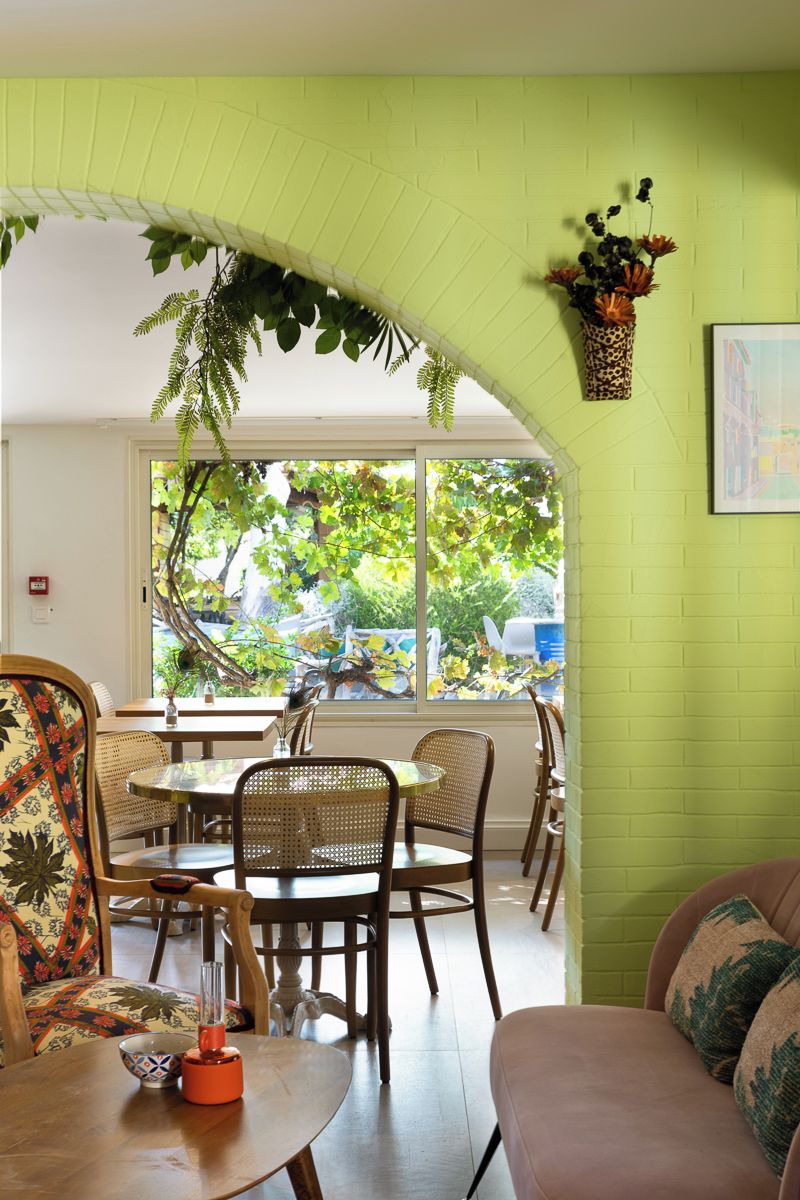 A dining area with a green brick wall, a window with a view of trees, and a hanging plant.