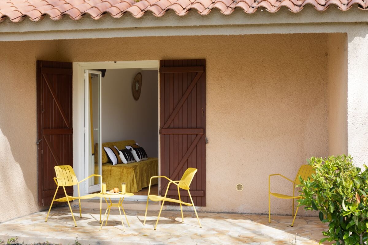 A patio with yellow chairs, a table, and a potted plant.