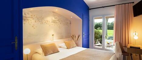 A bedroom with a large bed, a nightstand, a desk, and a view of the outdoors.