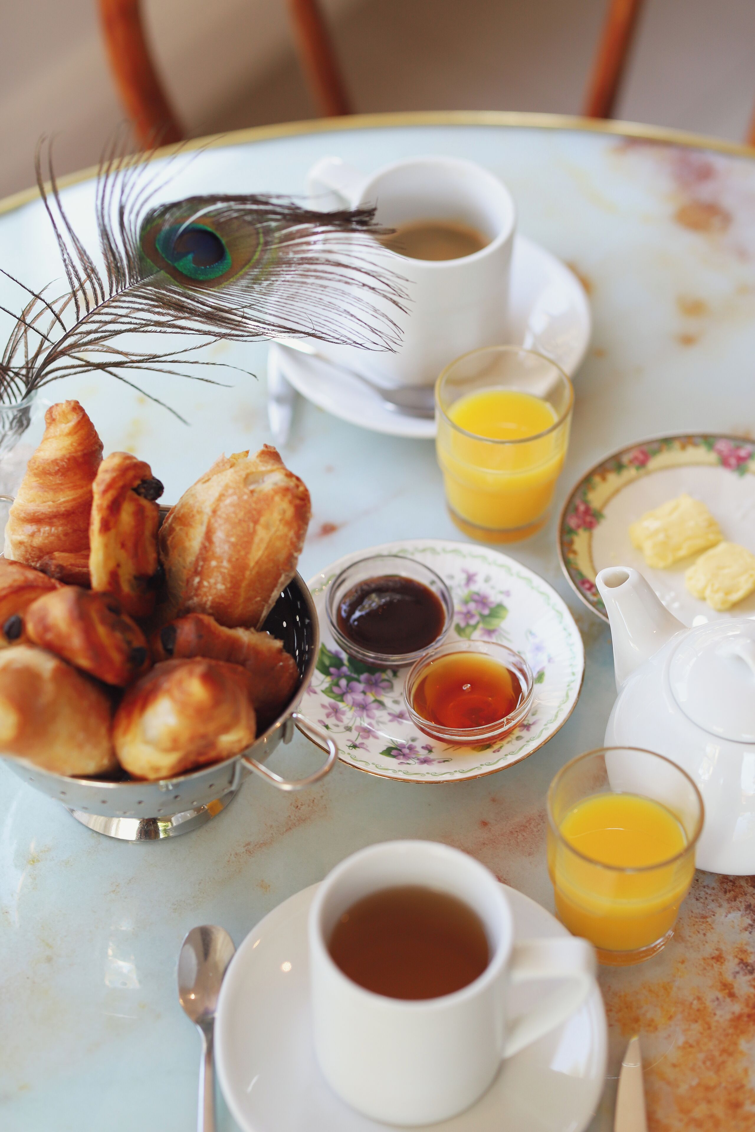 Une table de petit-déjeuner avec des croissants, du café, du jus de fruits et une théière.