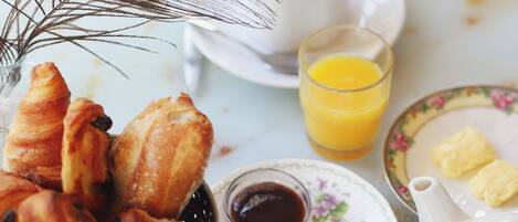 Una mesa de desayuno con cruasanes, café, jugo y una tetera.