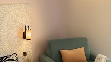 Um quarto com uma cama, uma poltrona verde, parede estampada e duas luminárias fixadas na parede.