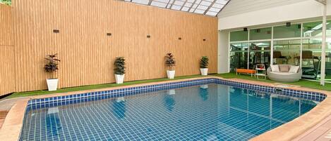 An indoor swimming pool with a wooden deck and a glass ceiling.