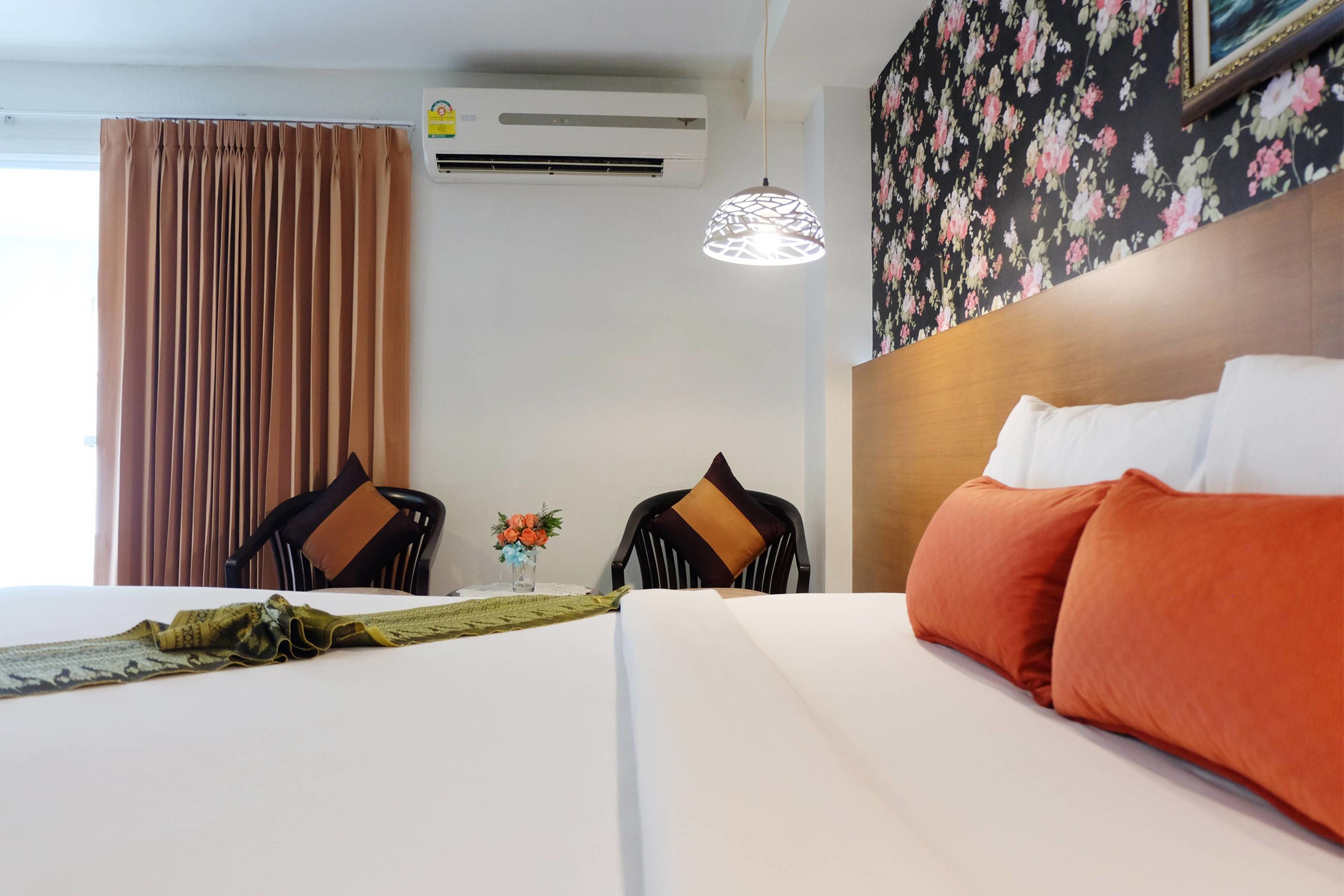 A hotel room with a bed, two chairs, a table with a vase of flowers, and a wall-mounted air conditioner.
