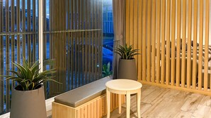 A modern room with a large sliding glass door, a wooden partition, a small round table, a bench, and two potted plants. - Grand Hill Resort and Spa (Nakhon Sawan)