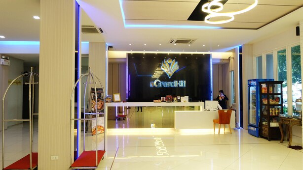 A hotel reception area with a GrandHill sign, a reception desk, a counter, a vending machine, and a chair. - Grand Hill Resort and Spa (Nakhon Sawan)
