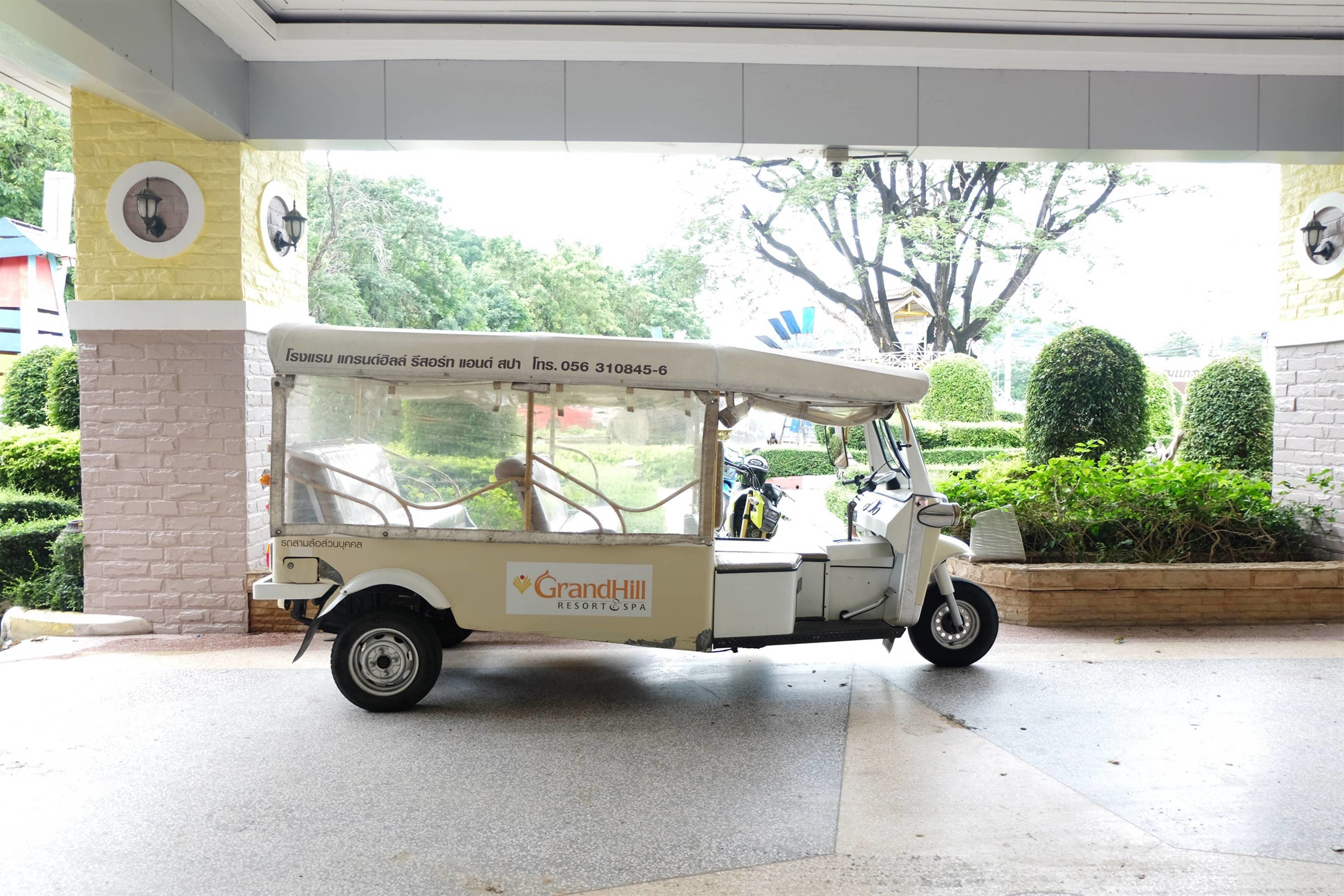 A white tuk-tuk parked at a resort entrance with a sign reading "GrandHill Resort & Spa".