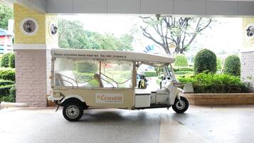 A white tuk-tuk parked at a resort entrance with a sign reading "GrandHill Resort & Spa".