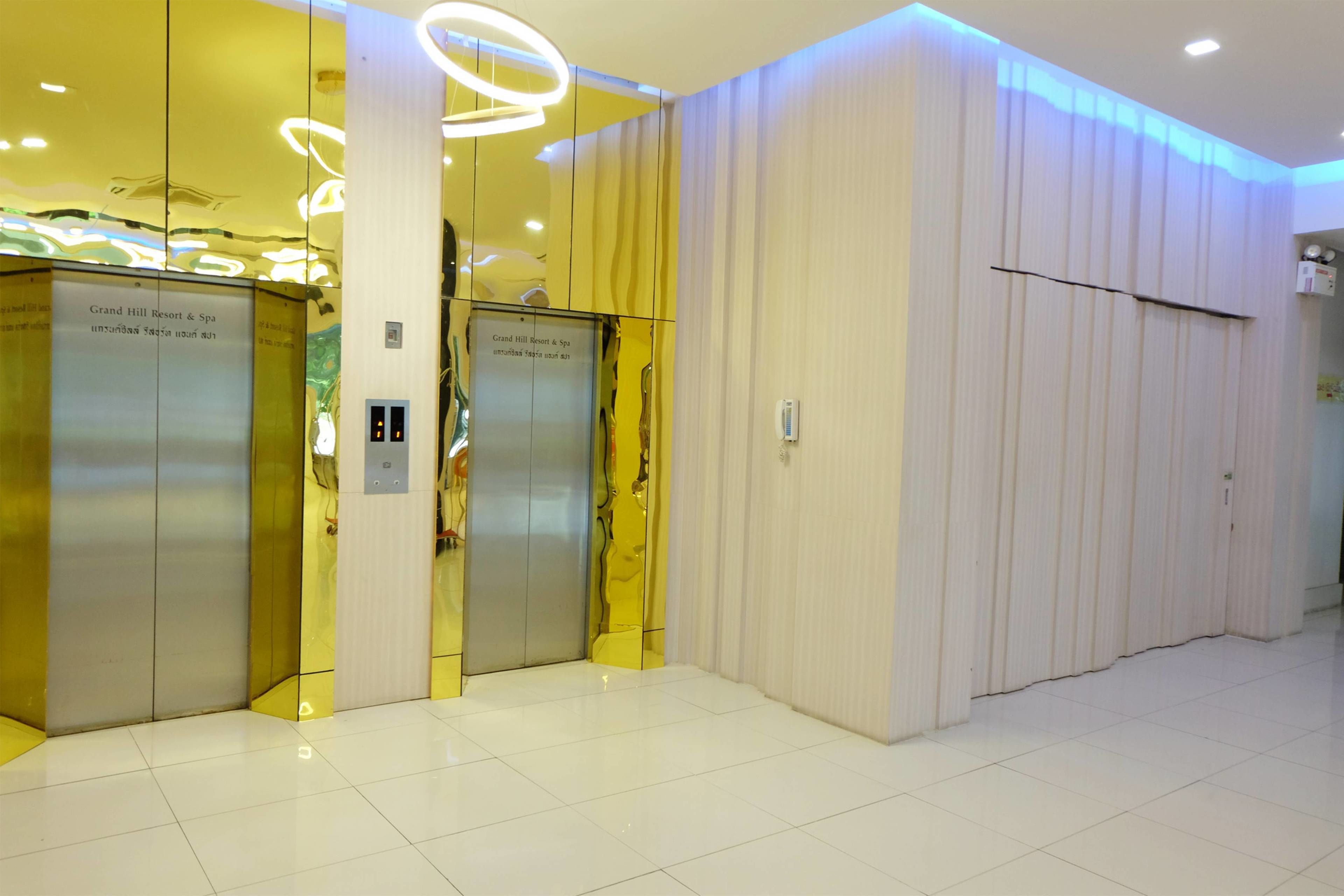 An elevator area with reflective surfaces and a sign indicating 'Grand Hill Resort & Spa'.