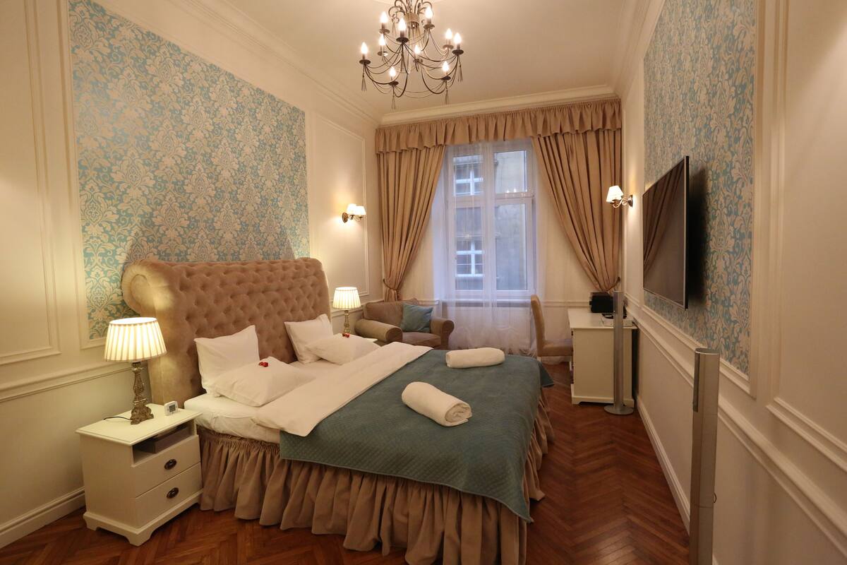 A bedroom with a large bed, a television, a nightstand, and a window with curtains.