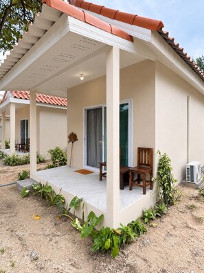 Um espaço ao ar livre coberto, com um alpendre, uma cadeira de madeira, uma mesa e um vaso de planta.