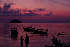 Ein Sonnenuntergang über einem ruhigen Meer mit Booten und einer kleinen Insel in der Ferne.