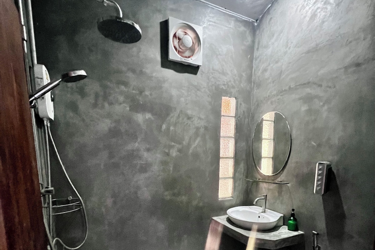 Une petite salle de bain aux dimensions réduites, avec un carrelage à motifs, des toilettes blanches, un lavabo surmonté d’un miroir et une pomme de douche.