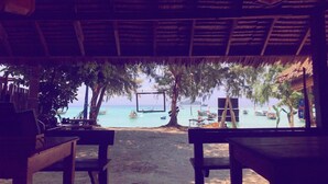 A beach view from a covered area with wooden benches and a thatched roof.