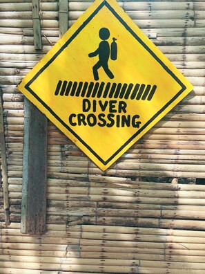 Ein gelbes, rautendes Schild mit einer schwarzen Silhouette einer Person, die einen Rucksack und eine Taucherbrille trägt, mit der Aufschrift "DIVER CROSSING".