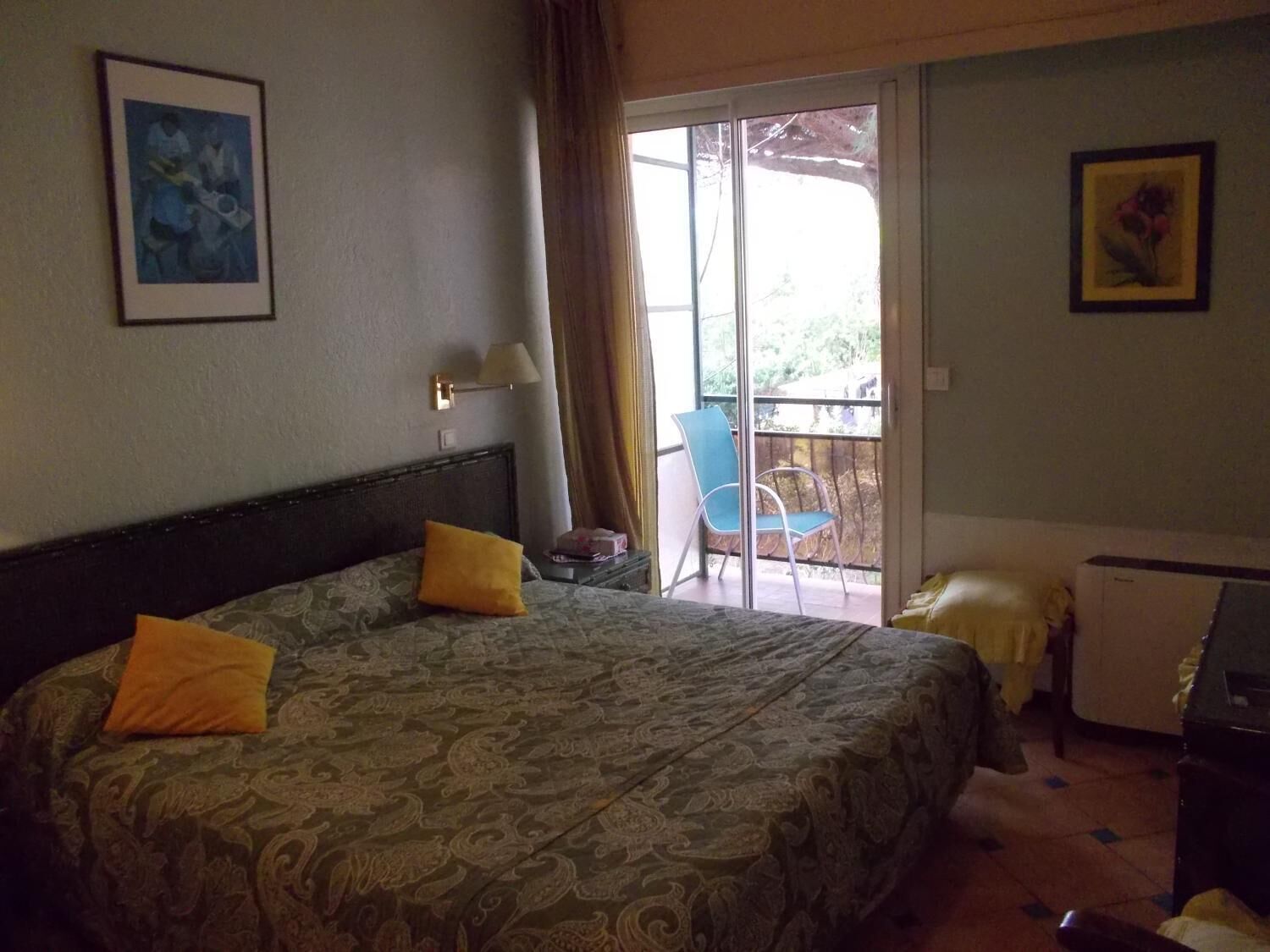 A hotel room with a large bed, a chair, a small table, and a balcony with a chair.