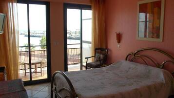 Habitación de hotel con cama, una silla, una mesa y vistas al mar a través de amplias ventanas.