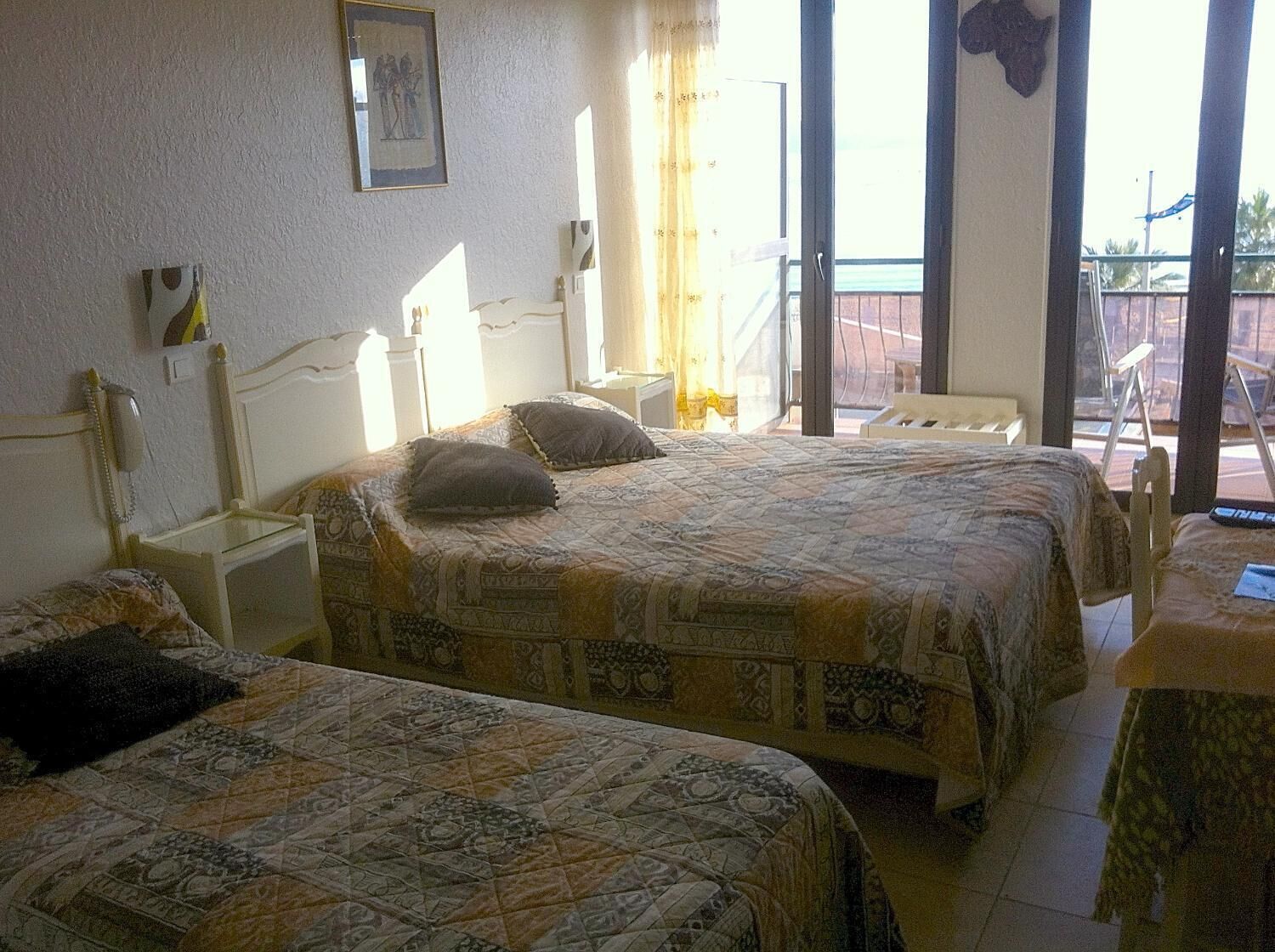 A hotel room with two beds, a small table, a chair, and a window with curtains.