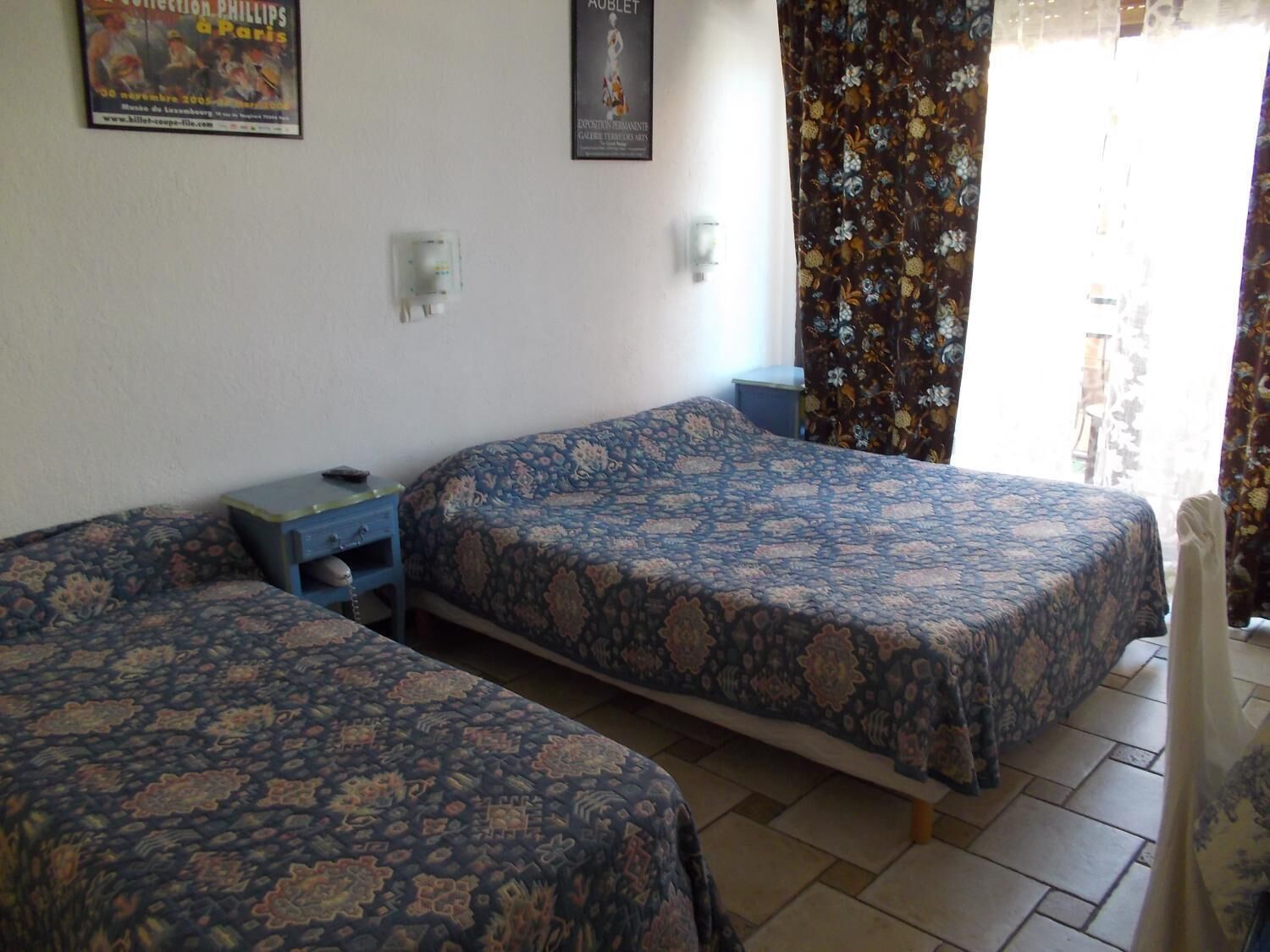 A room with two beds, a small table, and a wall-mounted light.