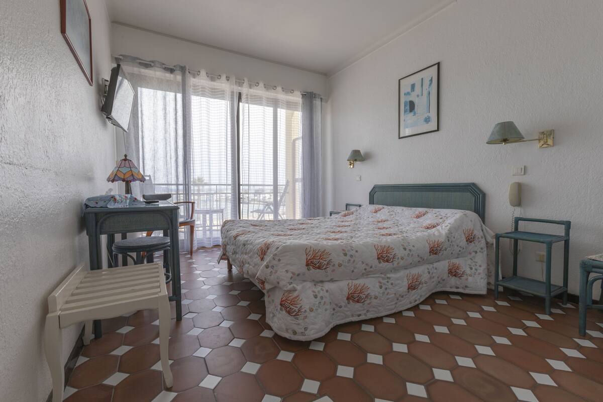 Ein Schlafzimmer mit Bett, Schreibtisch, Stuhl, einem kleinen Tisch und einem Balkon mit Blick.