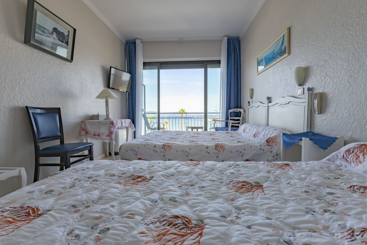 Ein Hotelzimmer mit zwei Betten, einem Sessel, einem Tisch und Meerblick.