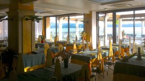 En restaurant med dækkede borde, store vinduer med havudsigt og et loft med ovenlys.
