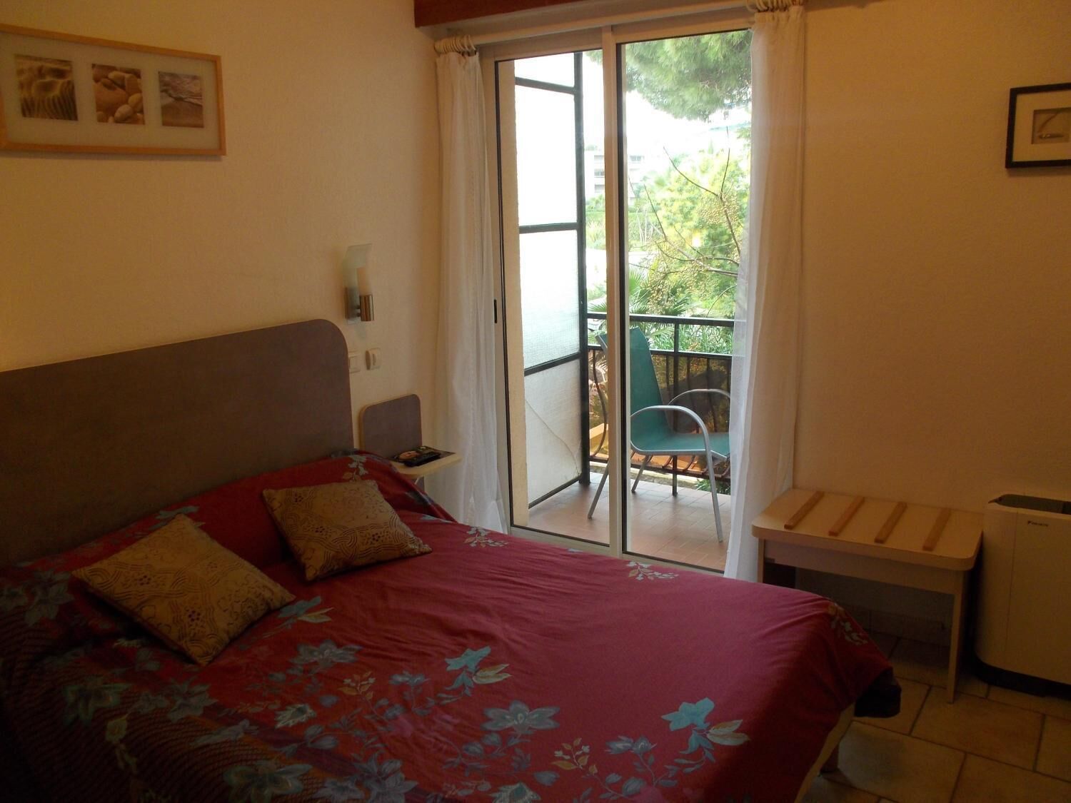 Un dormitorio con cama, una mesita y vistas a un balcón exterior.