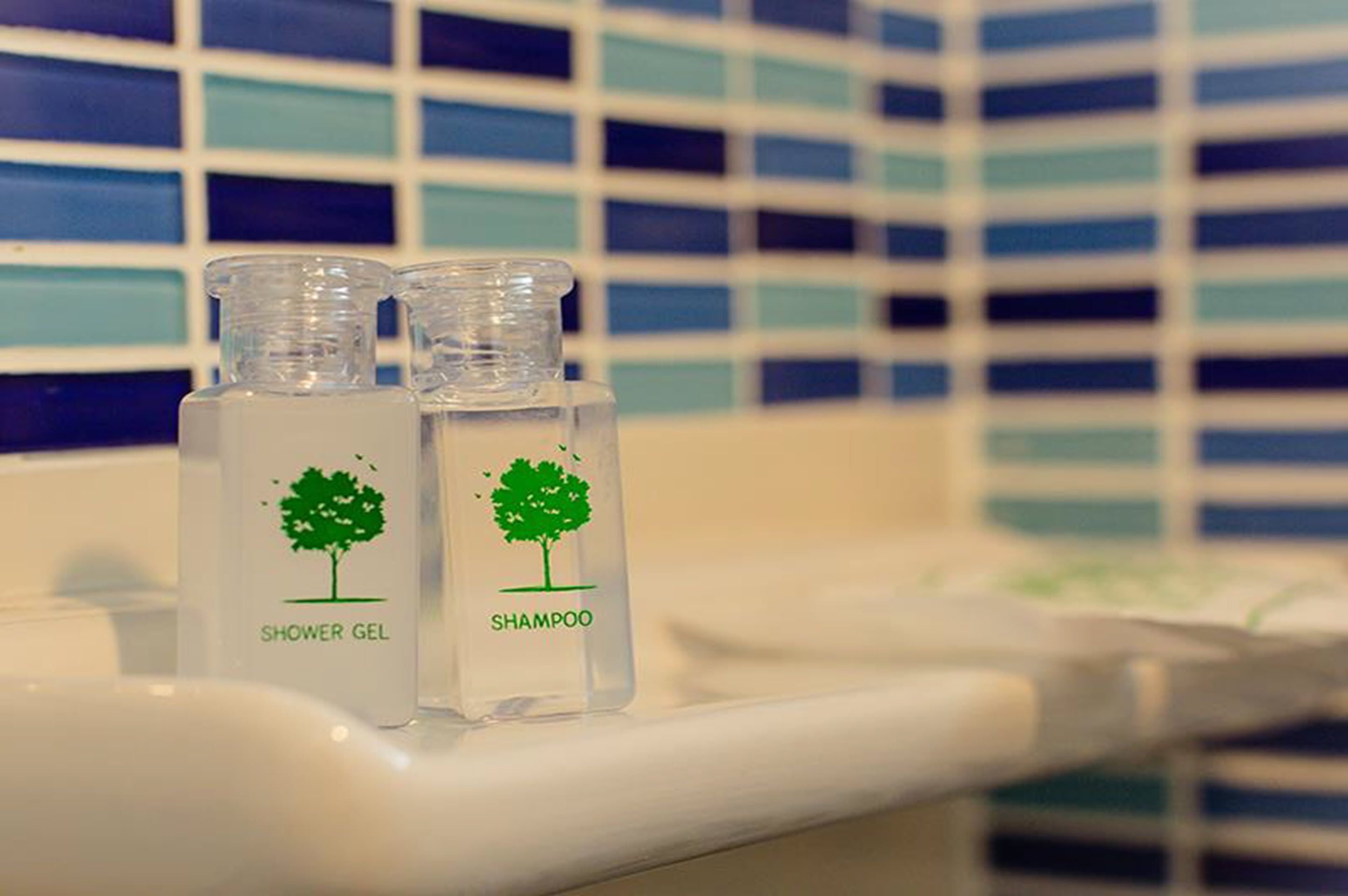 Duas embalagens transparentes com os dizeres 'gel de banho' e 'champô' numa bancada de casa de banho.