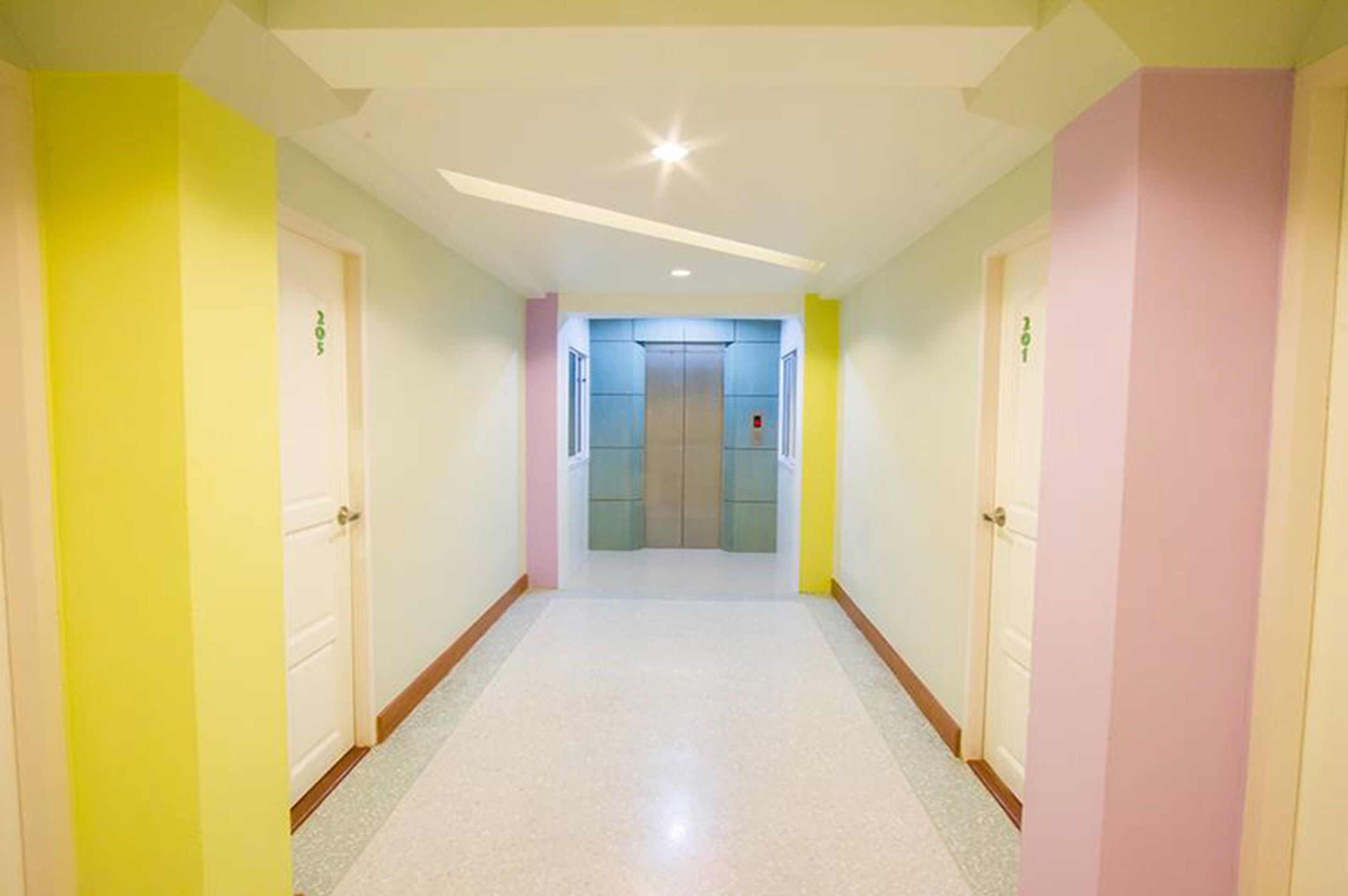 A brightly colored hallway with doors on either side and a central elevator area.