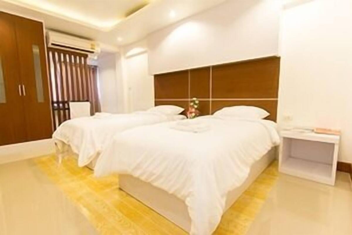 Ein modernes Hotelzimmer mit zwei Betten, einem Holzschrank, einem Nachttisch und einem kleinen Beistelltisch.