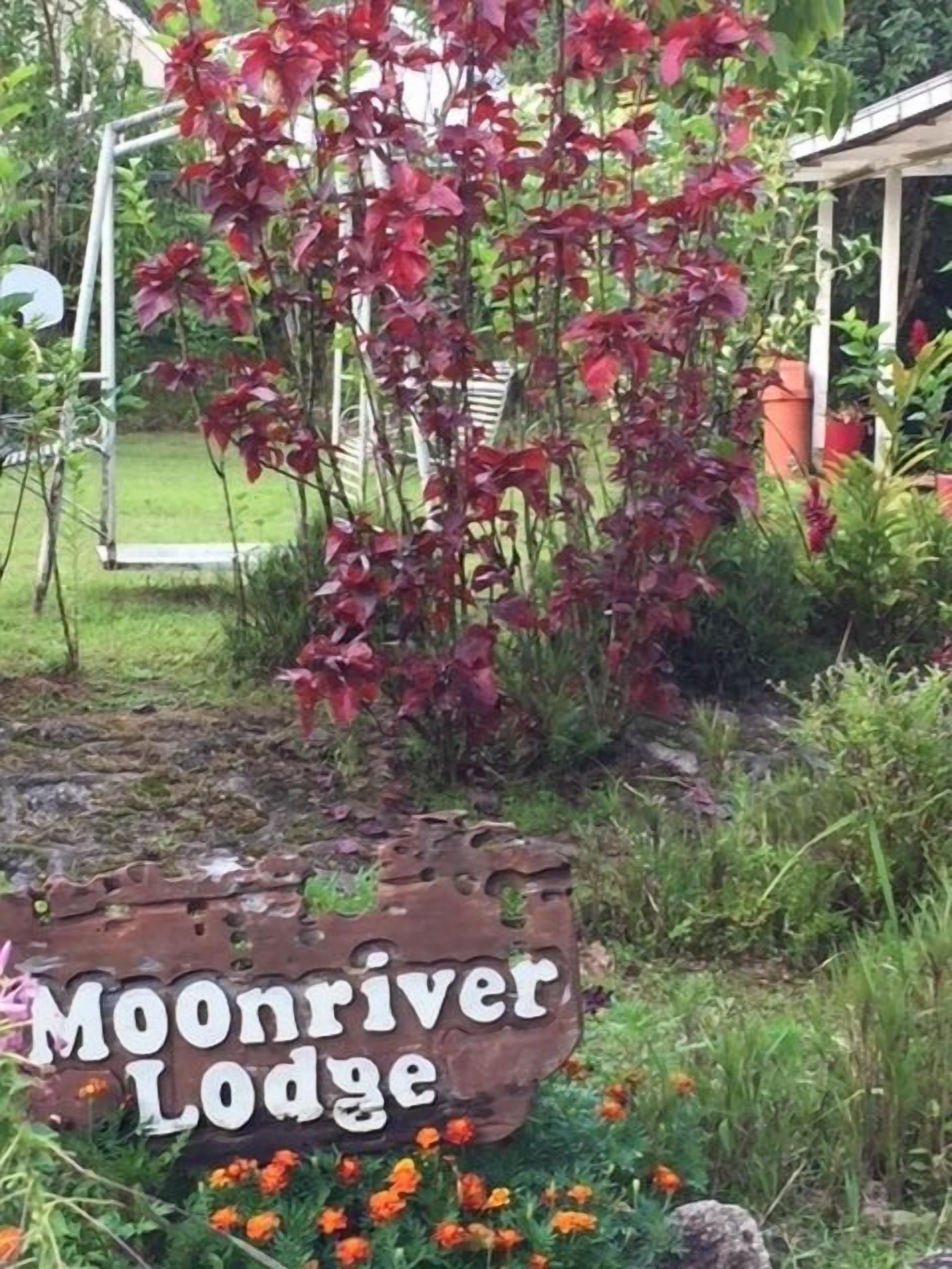 A sign for Moonriver Lodge with a rustic design, surrounded by a garden with various plants and flowers.