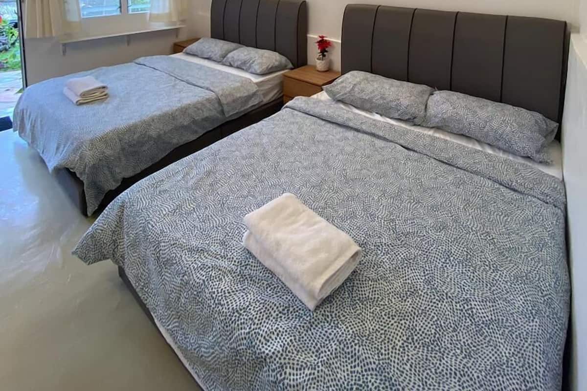 A hotel room with two beds, a ceiling fan, a window with curtains, and a bedside table with a vase of flowers.