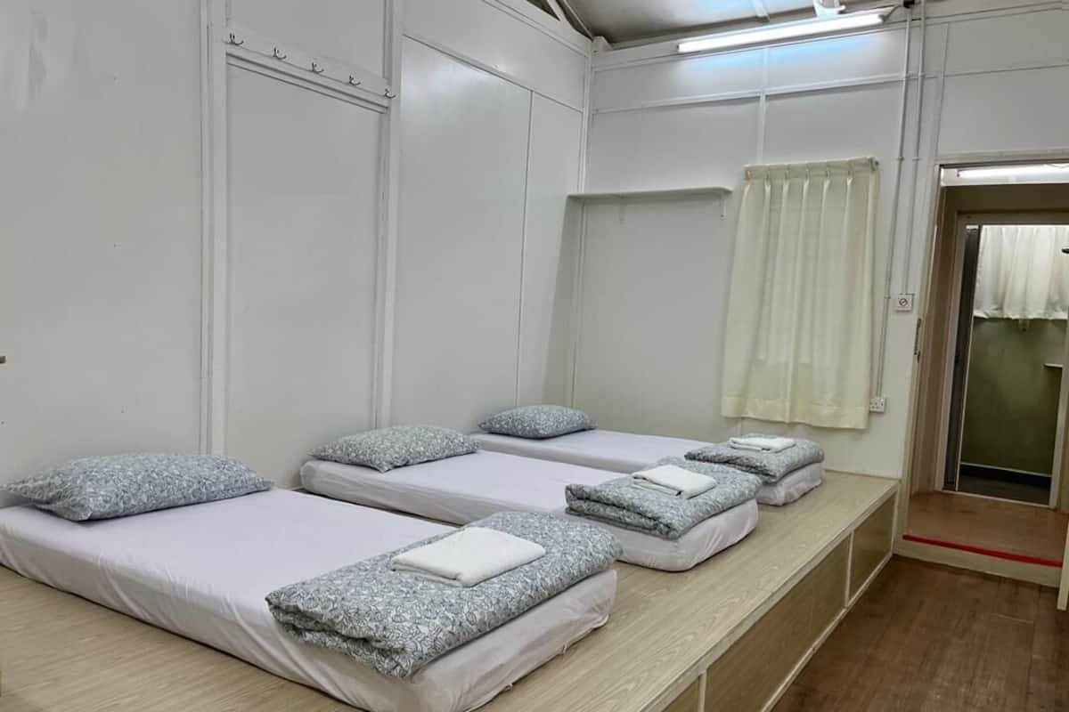 A room with four single beds, each with a patterned pillow and a folded towel.
