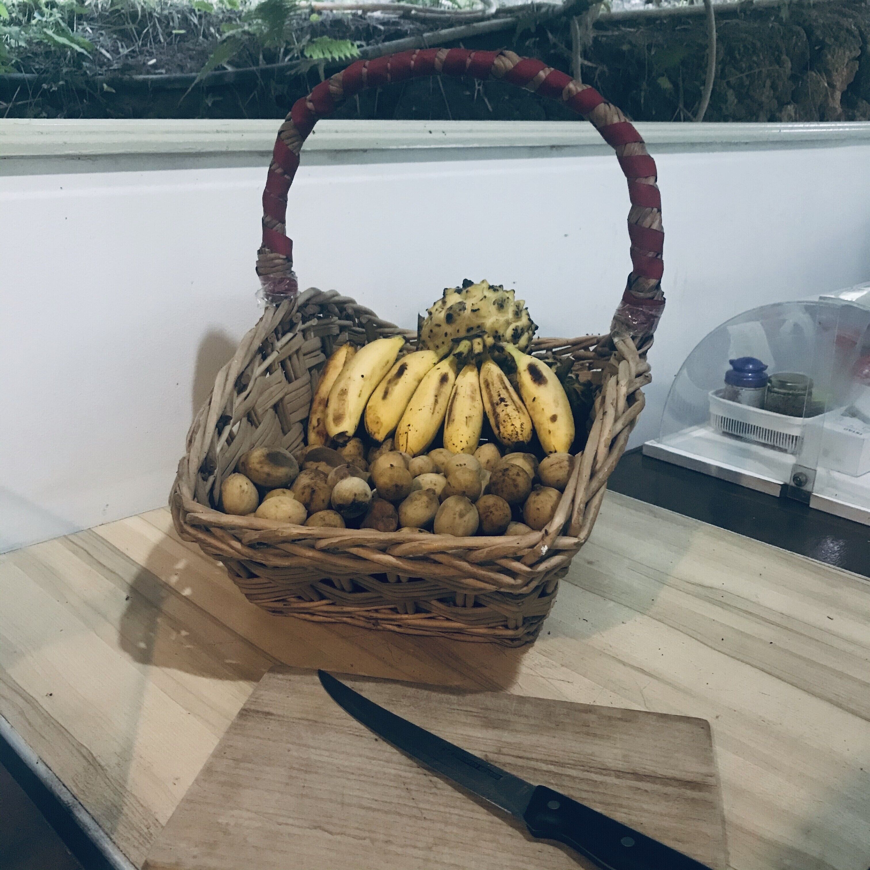 A wicker basket filled with bananas and potatoes on a wooden surface.