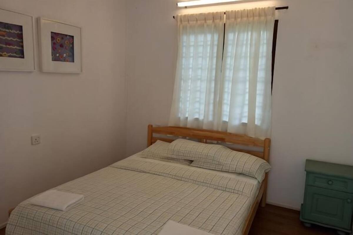 A bedroom with a bed, a nightstand, a window with curtains, and two framed pictures on the wall.
