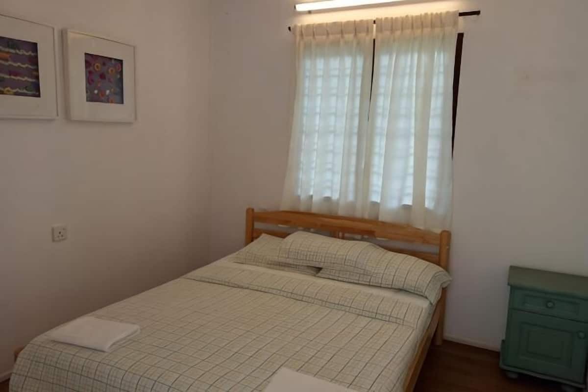 A bedroom with a bed, a nightstand, a window with curtains, and two framed pictures on the wall.