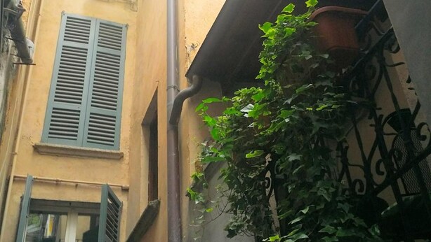 Un estrecho callejón con un edificio que presenta una ventana con persianas, una puerta y un pequeño balcón con una planta en maceta.