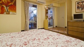 Un dormitorio con cama, armario, televisor y puerta que da a un balcón.
