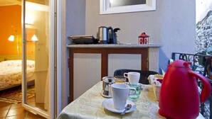 Un pequeño comedor con una mesa dispuesta para dos personas, una tetera roja y una ventana sobre la mesa.