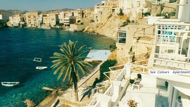 A coastal view with buildings, a palm tree, and boats on the water.