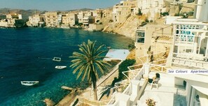 Vista costera con edificios, una palmera y barcos en el agua.