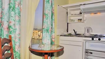 A compact kitchen with a view of a cityscape through a window, a small table, and a chair.