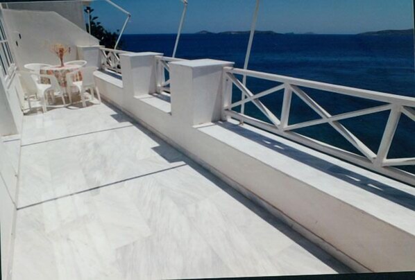 A white deck with a table and chairs, overlooking the sea.