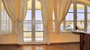 A room with large windows, wooden flooring, and a view of a balcony with railings.