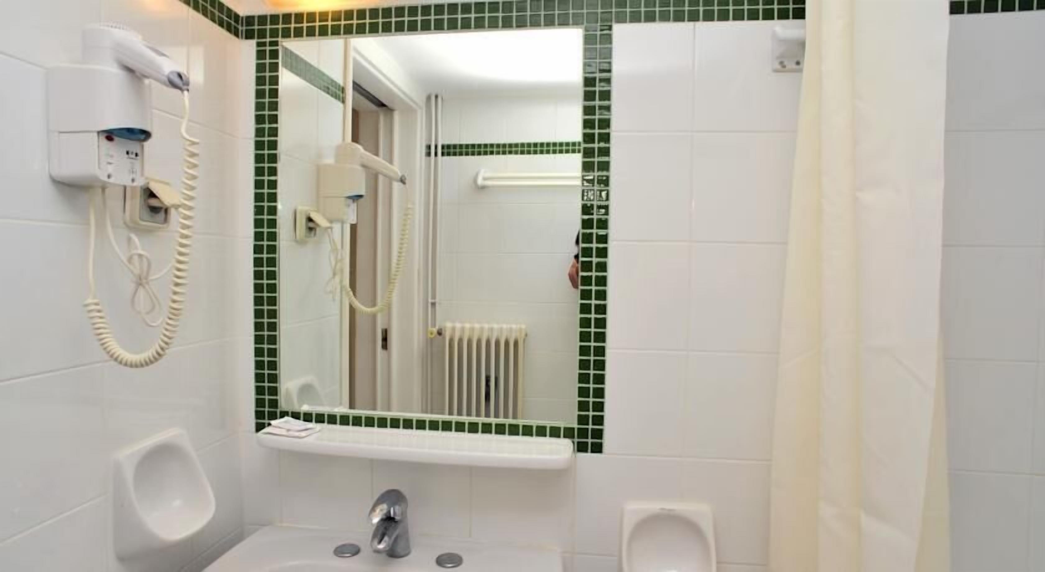 A bathroom with a urinal, a sink, a mirror, and a hairdryer mounted on the wall.
