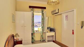 Habitación de hotel con cama, escritorio con televisor, armario, ventana con cortinas y vista a la ciudad.